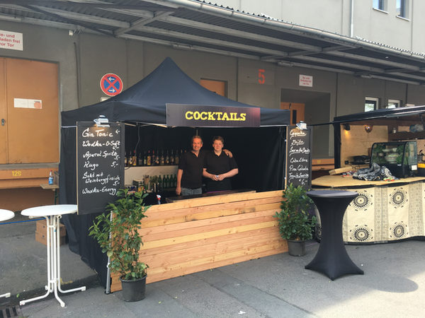 Zwei Barkeeper hinter einem Cocktail-Stand mit Holzfront
