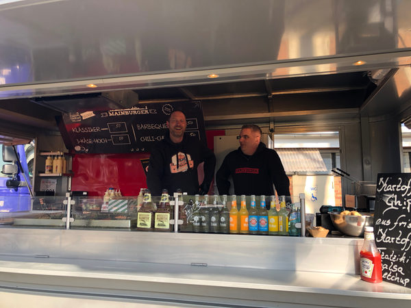 Zwei Männer stehen lächelnd in einem Foodtruck